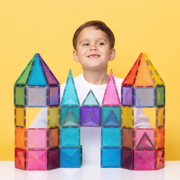 Child playing with Connetix New Glitter Castle Pack colorful magnetic building blocks shaped like a castle on a yellow background