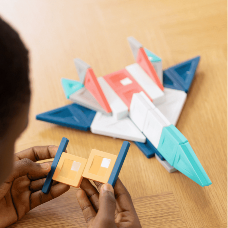 Child playing with colorful Connetix Magnetic Tiles New Pro Pack in geometric shapes on a wooden table